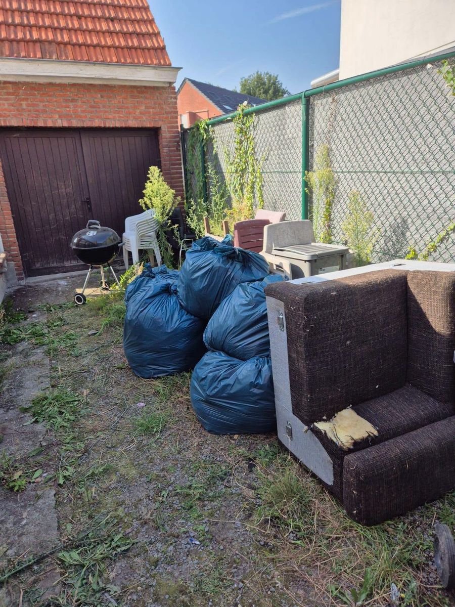 Zijkant van de woning met zakken, een zetel en ander afval voor de opruiming